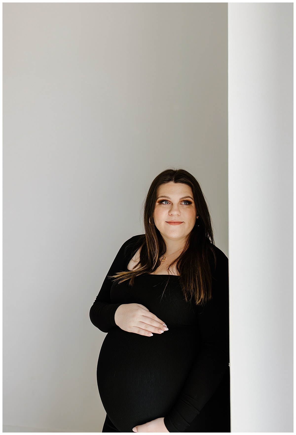 Woman stands holding her belly during their studio maternity session