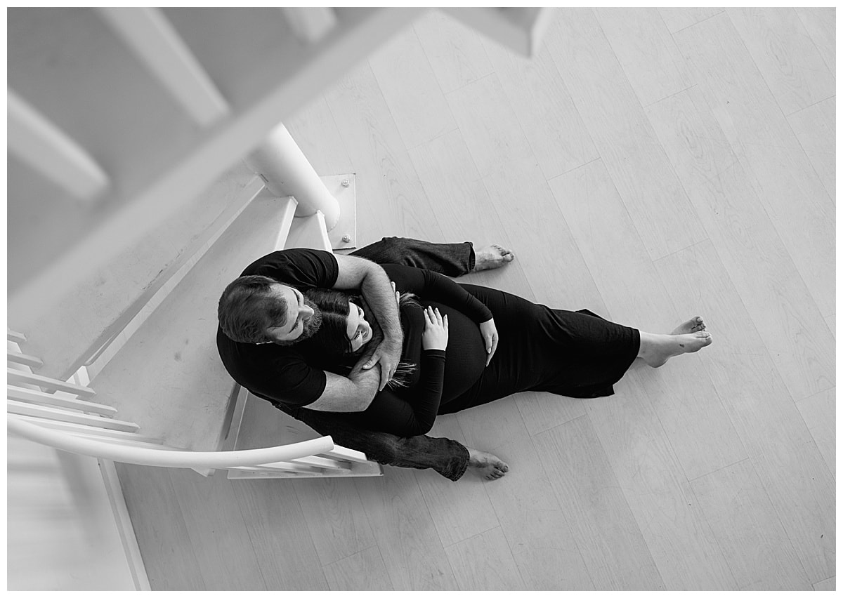 Man and woman sit on the edge of the stairs hold each other for their studio maternity session