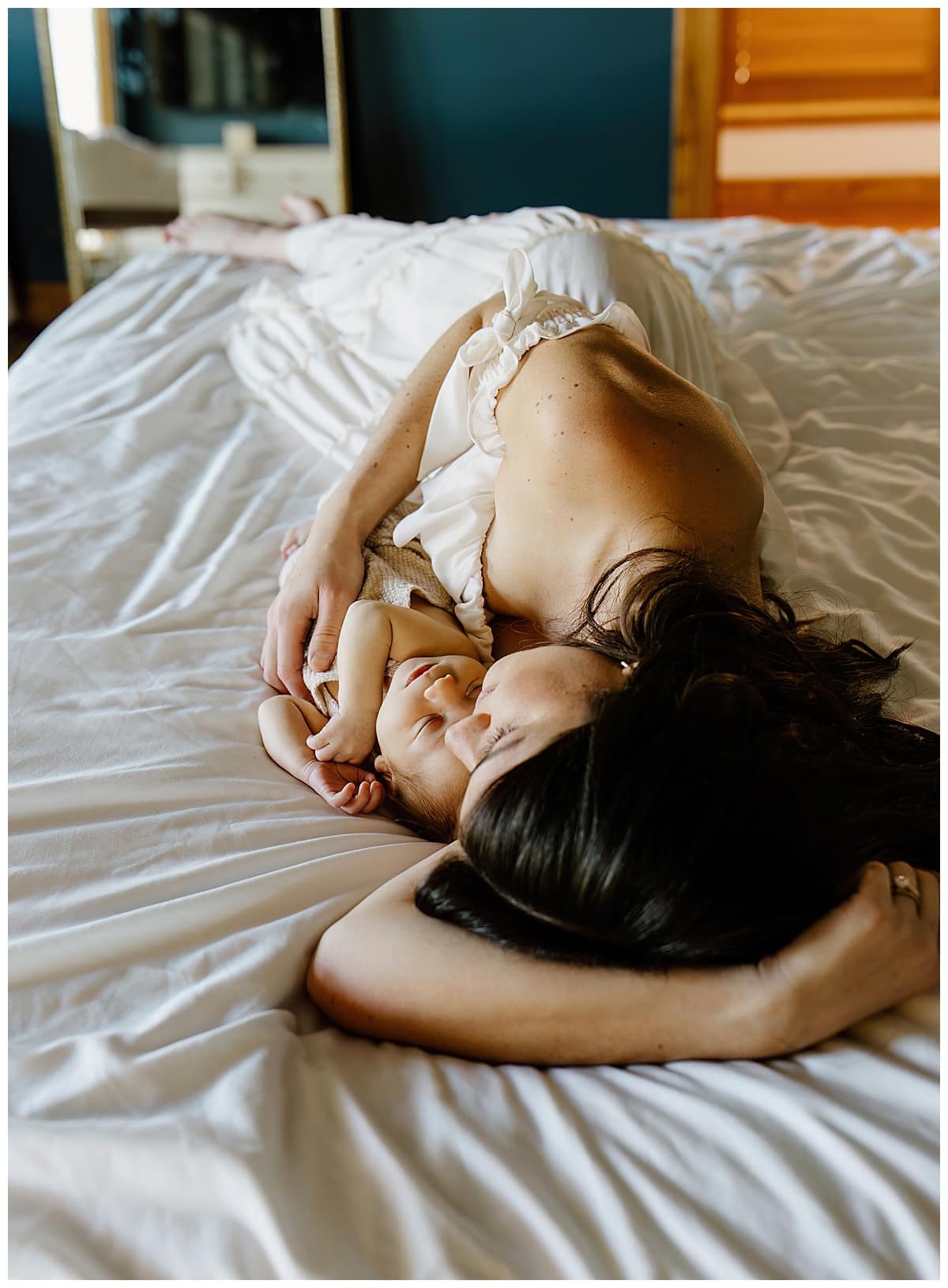 Mom lays with young infant on the bed for Austin Motherhood Photographer