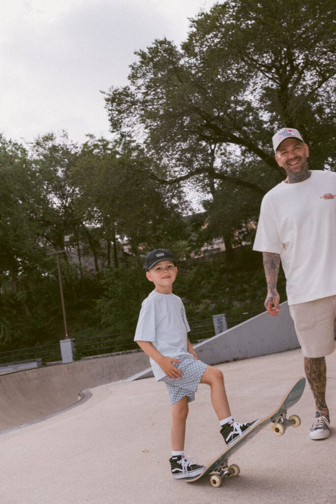 Austin family photographer captures a smiling father and young son with a skateboard at an outdoor skatepark.