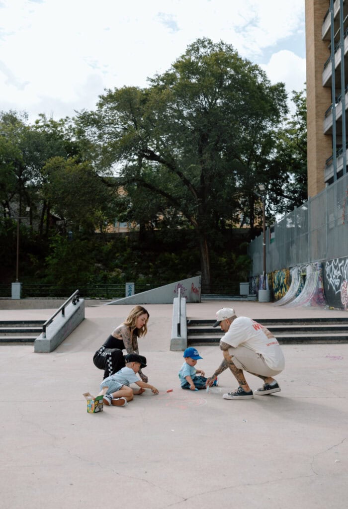 Austin family photographer captures parents and two young sons drawing with sidewalk chalk at an outdoor skatepark.