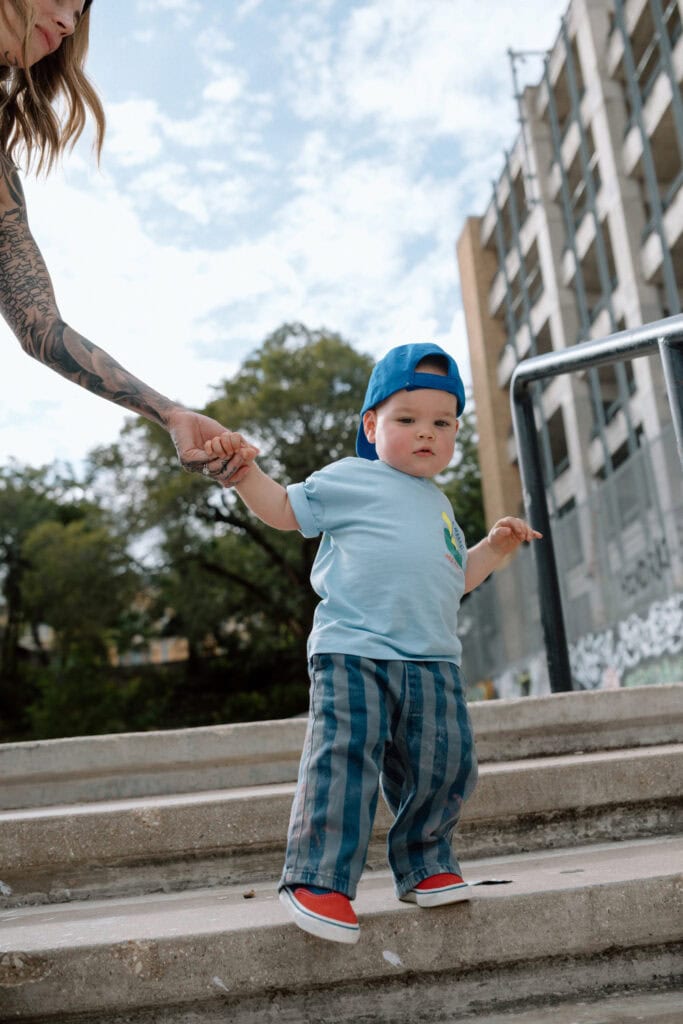 Toddler in a blue baseball cap holding his mother's hand while walking down concrete steps.