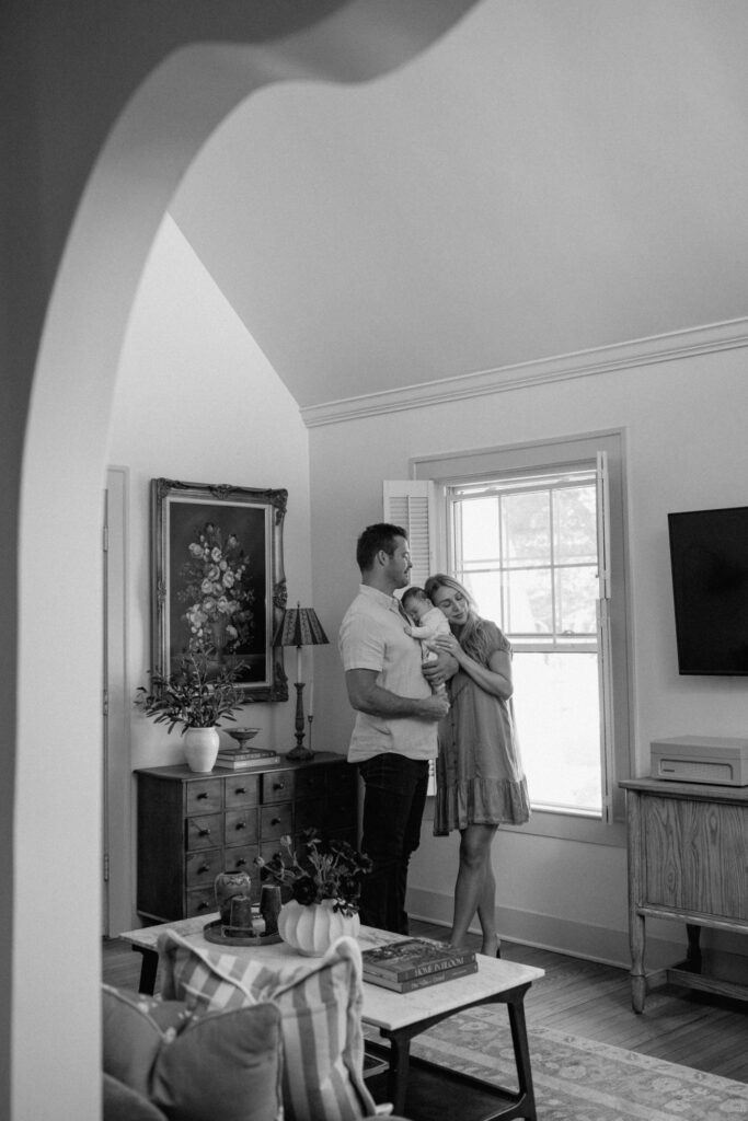 Black and white Austin newborn photography of parents holding their baby, framed by an archway.