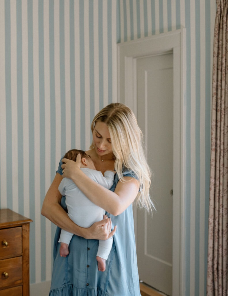 Mom in a blue dress snuggles her baby close during an Austin newborn photography session.