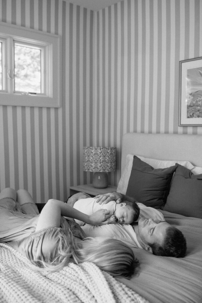Baby sleeps on dad’s chest as parents lie on the bed during Austin newborn photography.
