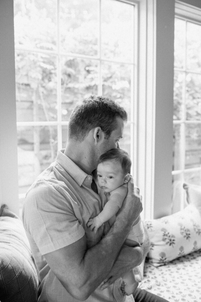 Dad holds his baby close by a window in black and white Austin newborn photography.