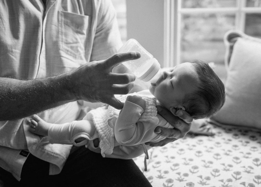 Black and white close-up of dad cradling his baby’s head while feeding a bottle.